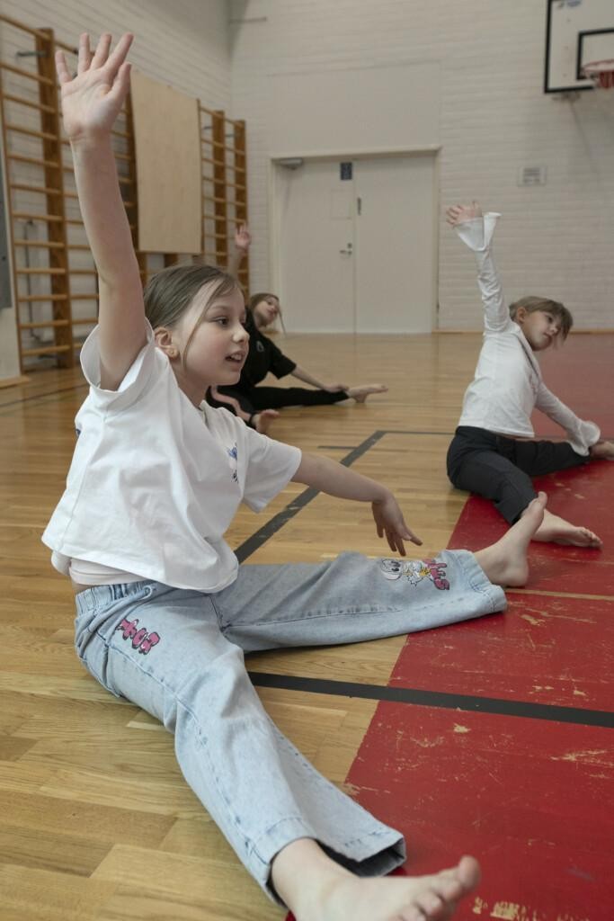 Lapset istuvat liikuntasalin lattialla ja venyttelevät.